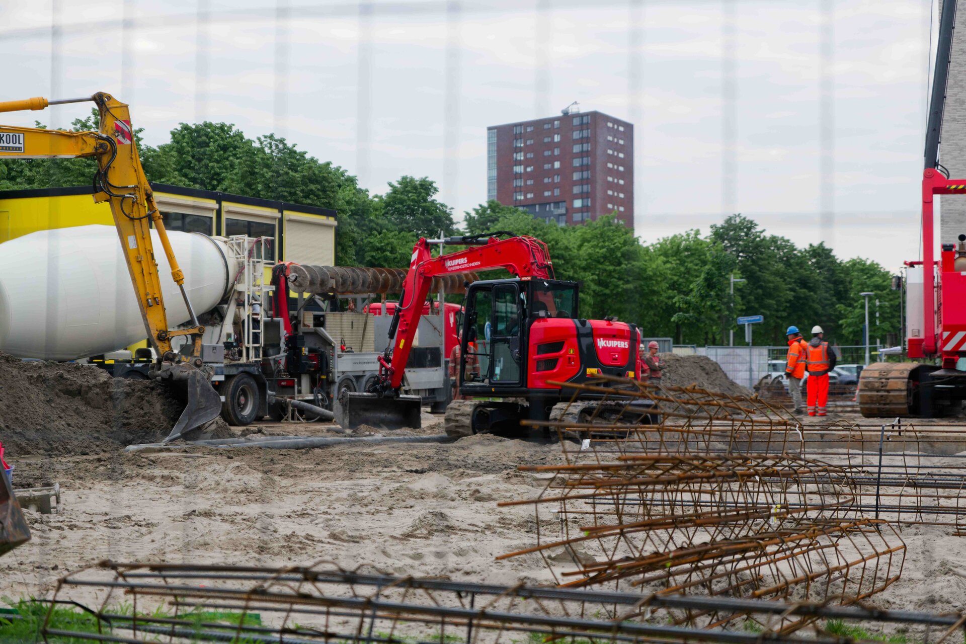 Wide site view: concrete mixer, Kuipers excavator and rebar cages